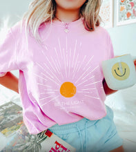 Load image into Gallery viewer, Person wearing a pink t-shirt with a sun design and text, holding a smiley face mug.
